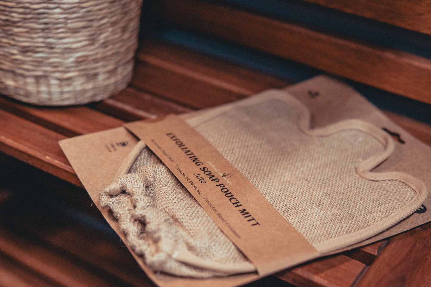 Bath mitt and soap pouch on a wooden surface with a wicker basket in the background.